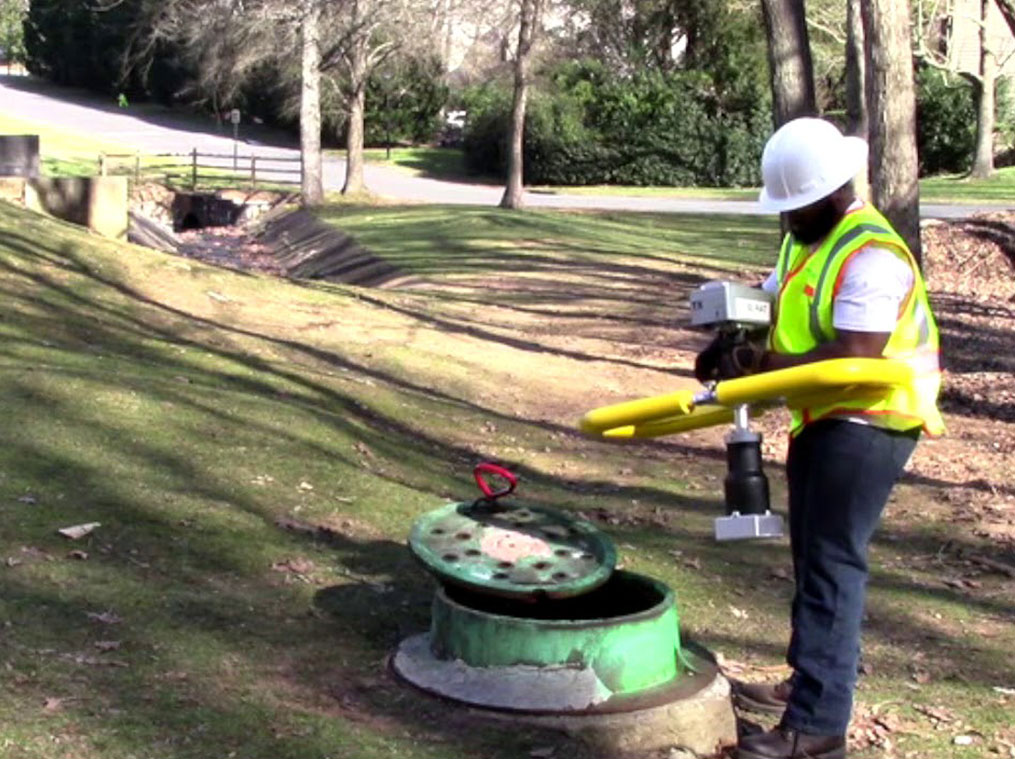Sewer worker reading SL-RAT data near a manhole.