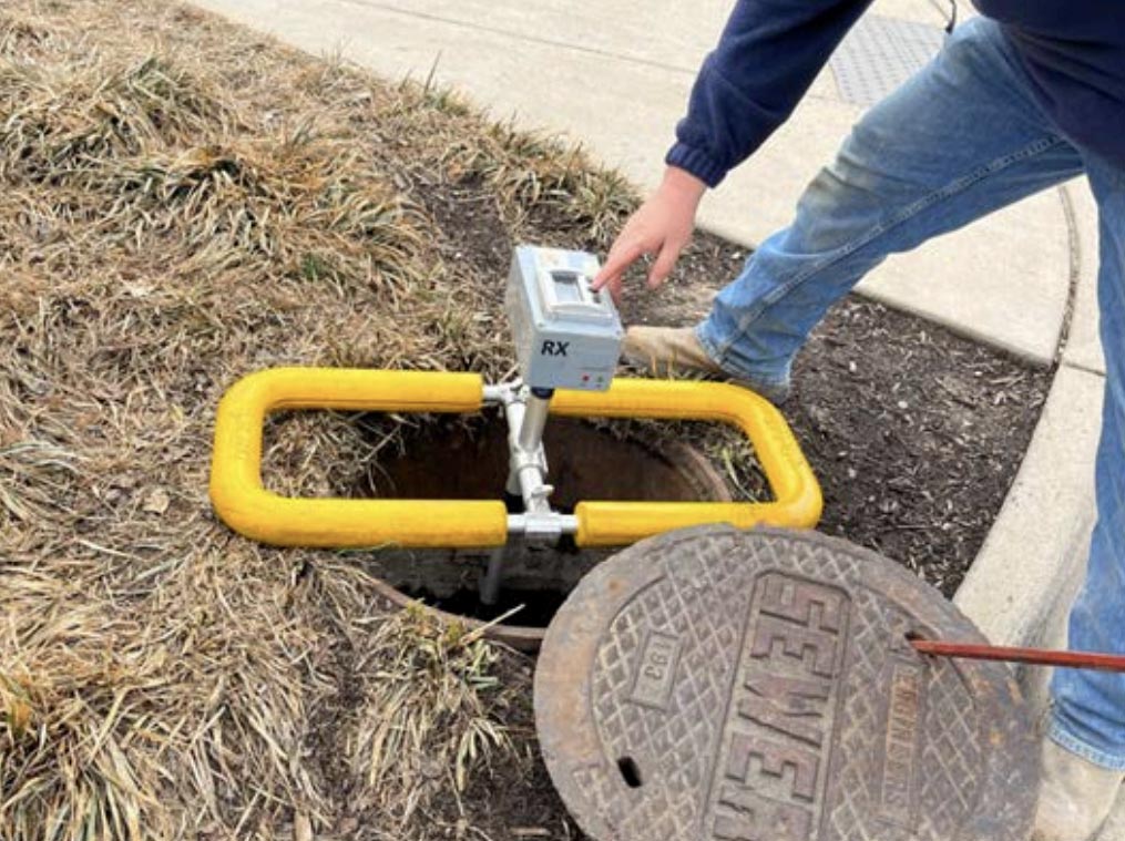 person bending down over manhole cover placing an SL-RAT transmitter device