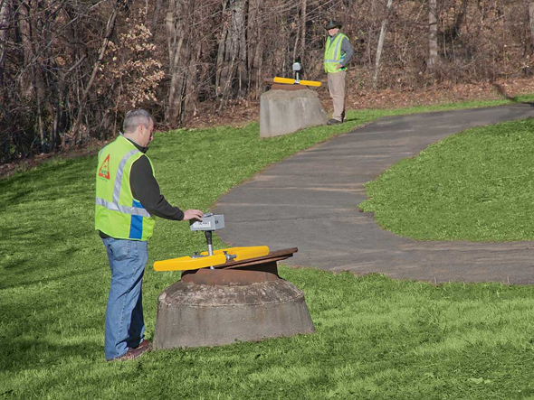 Two people over manholes, with the SL-RAT transmitter and SL-RAT receiver devices
