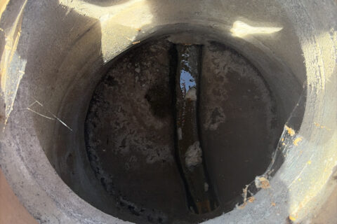 View looking down into a concrete manhole showing two intersecting pipes at the bottom, with some dirt and moisture visible inside.